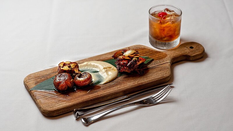 Appetizer served on a board with an Old Fashioned cocktail.