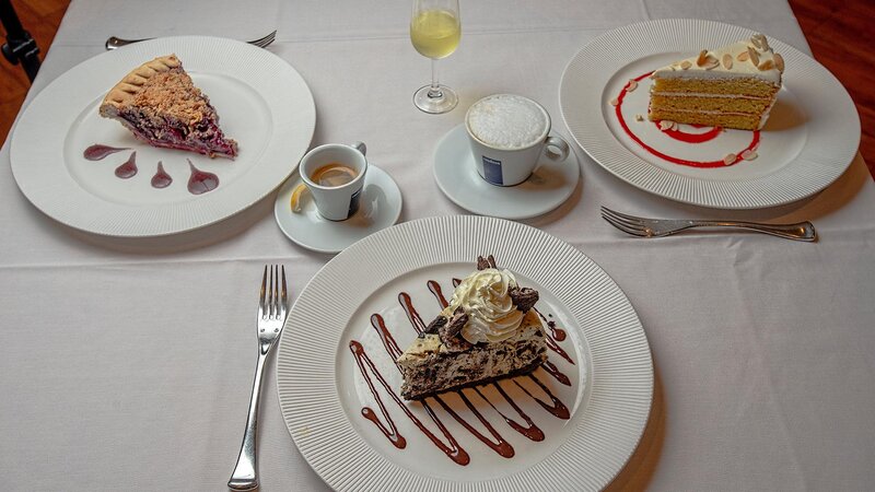 Multiple cake and pie desserts. Cappuccino, espresso and white wine. Table setting for three.
